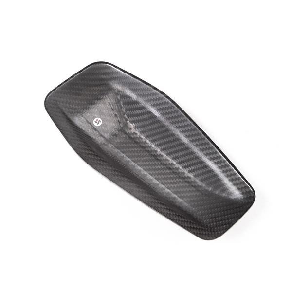 A carbon fiber panel with textured weave pattern lies flat against a plain white background, featuring a small, circular decal near its center.