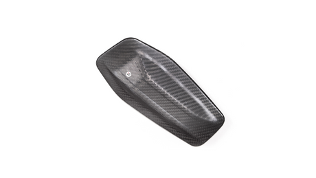 A carbon fiber panel with textured weave pattern lies flat against a plain white background, featuring a small, circular decal near its center.
