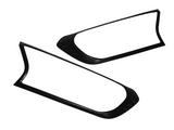 Two black, elongated plastic frames with rounded edges, possibly for vehicle lights, lay on a white background. Each frame features minor indents near one end, adding subtle detailing.