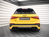 Yellow Audi RS3 car, stationary, viewed from the rear in a showroom with checkered gray flooring and white-striped walls. Text: 