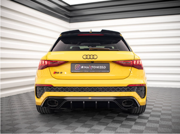Yellow Audi RS3 car, stationary, viewed from the rear in a showroom with checkered gray flooring and white-striped walls. Text: "#MAXTONIZED."