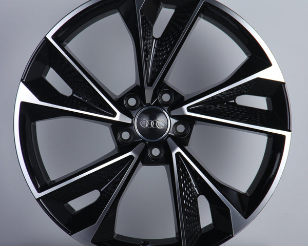 A black and silver alloy wheel with a geometric design and five dual spokes is displayed upright on a neutral background. The center features a logo with four interlocking rings.
