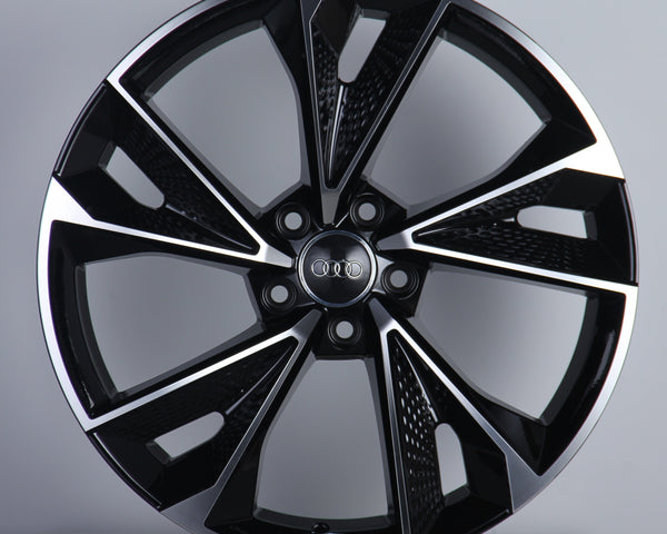 A glossy black alloy wheel with silver accents featuring five wide spokes and a central emblem displaying four interlocking rings. It is displayed on a plain gray background.