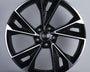 A glossy black alloy wheel with silver accents featuring five wide spokes and a central emblem displaying four interlocking rings. It is displayed on a plain gray background.