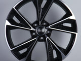 A black and silver alloy wheel is displayed upright, featuring a modern design with multiple spokes. The 