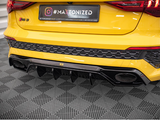 A yellow car's rear bumper, featuring dual exhausts and a honeycomb pattern, sits on a checkered floor. Text on a sign reads, “#MAXTONIZED” and contact details for 