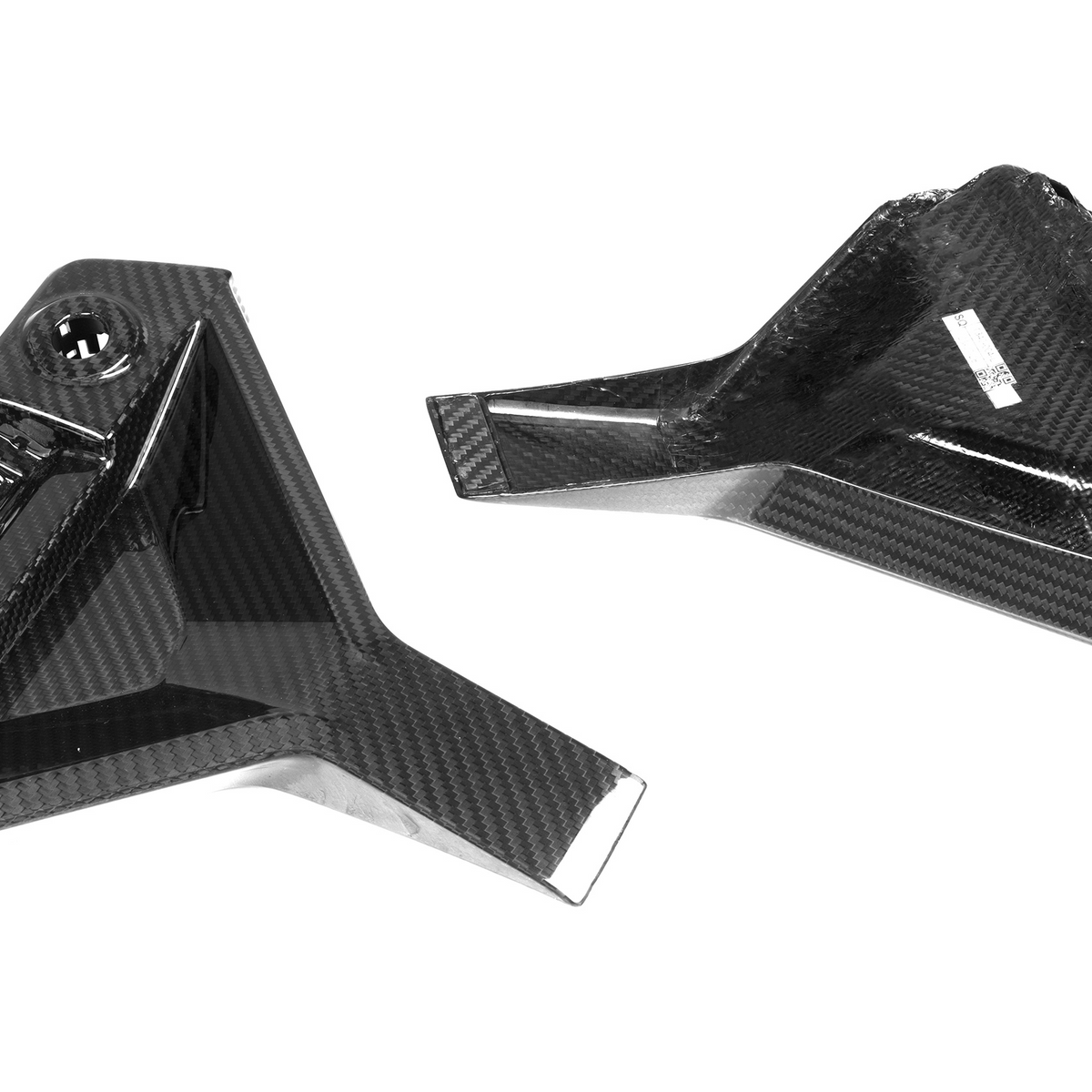 Carbon fiber components lying on a white surface; one has a rectangular grid pattern, and the other features mounting clips and a small label.
