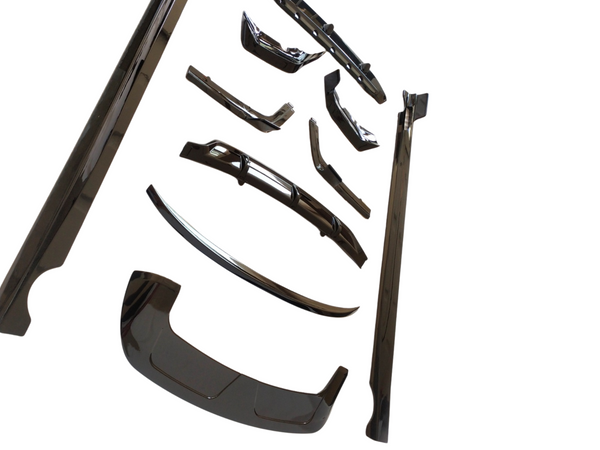 Assorted shiny black car body parts, including bumpers and trim pieces, are neatly arranged on a white background, emphasizing their polished surfaces and intricate designs.
