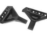 Two carbon fiber car parts, featuring angular designs with multiple slots and a bolt hole, are positioned against a plain white background.