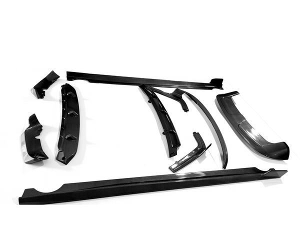 Various carbon fiber car parts lie scattered on a white surface, including spoilers and side skirts, arranged in an orderly fashion, highlighting their sleek, aerodynamic design.