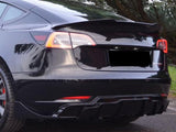 A sleek, black car with tinted windows is parked on a road, surrounded by green trees. The rear design includes distinct taillights and a spoiler, conveying a modern, sporty appearance.