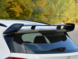 A sleek car spoiler perched on the rear of a white vehicle, situated against a backdrop of green and yellow foliage on a clear day.