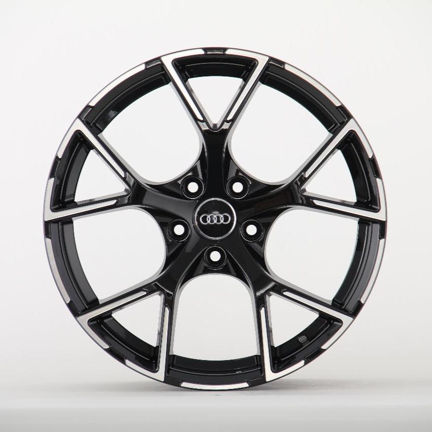A black alloy wheel rim with a five-spoke design and the Audi logo at the center, resting against a plain white background.