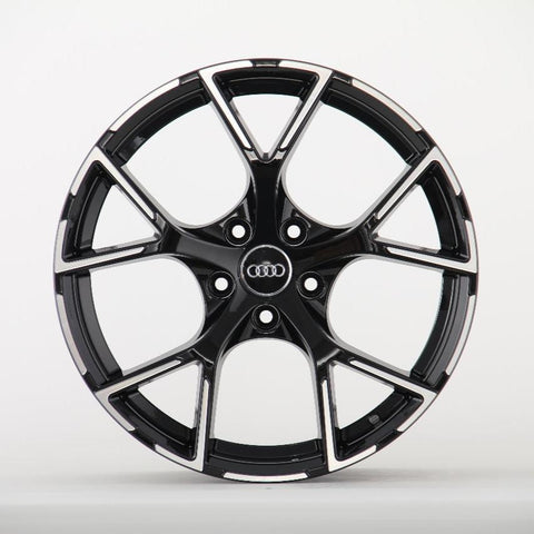 A black alloy wheel rim with a five-spoke design and the Audi logo at the center, resting against a plain white background.