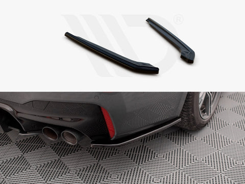 Two black car parts displayed above an installed piece on a car's rear bumper near dual exhaust pipes. The car is parked on a patterned surface.