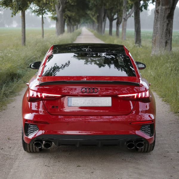 A red Audi S9 is parked on a narrow dirt road flanked by tall trees and lush greenery, under a cloudy sky.
