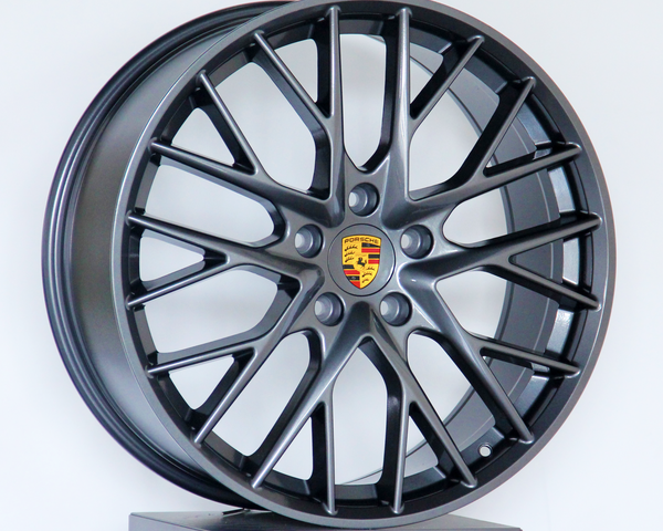 A dark alloy wheel with a multi-spoke design and a central Porsche logo is displayed upright against a plain white background.