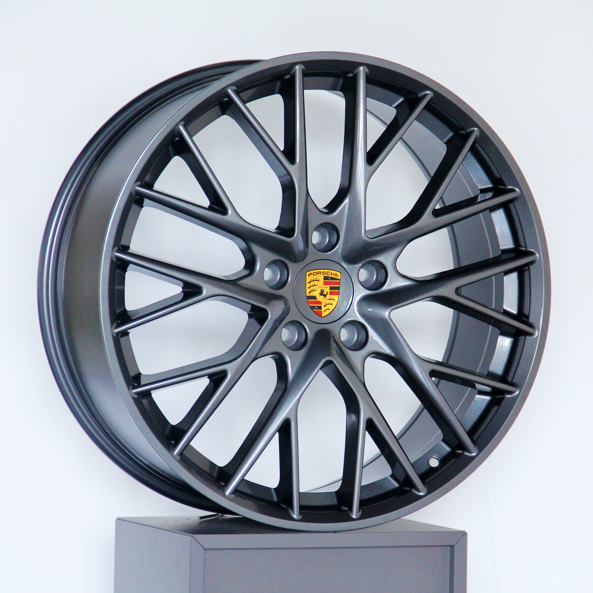 A dark alloy wheel with a multi-spoke design and a central Porsche logo is displayed upright against a plain white background.