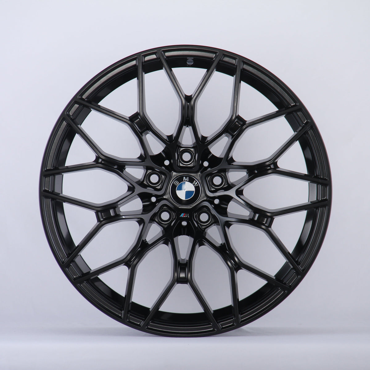 A black alloy wheel with a complex, multi-spoke design is displayed against a plain white background. The center features the BMW logo, surrounded by intricate patterns.