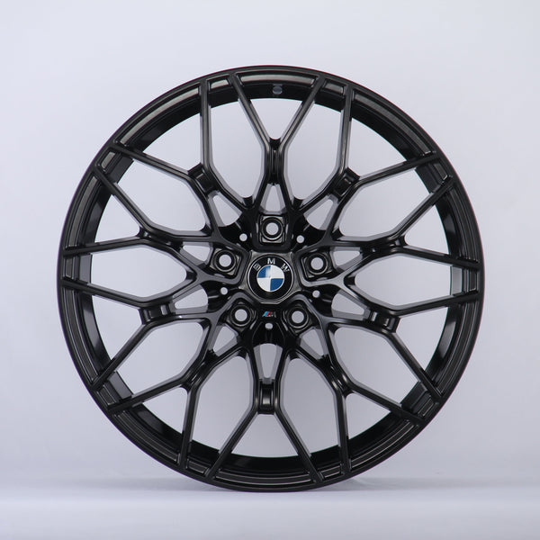 A black alloy wheel with a complex, multi-spoke design is displayed against a plain white background. The center features the BMW logo, surrounded by intricate patterns.