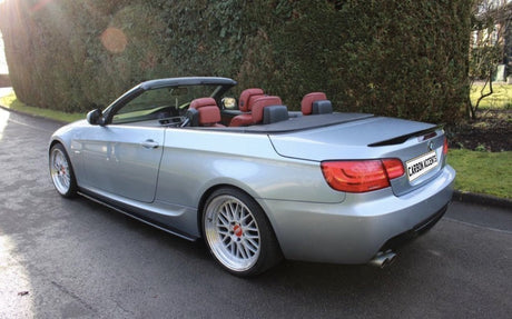 Convertible car parked, top down revealing red interior, surrounded by hedge and grass. License plate reads "CARBON ACCENTS."
