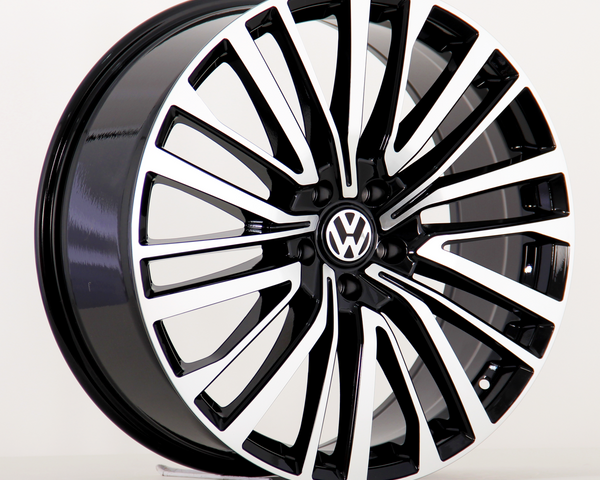 A car wheel features a black and silver multi-spoke design with a central Volkswagen emblem, displayed against a plain white background.