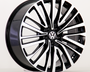 A car wheel features a black and silver multi-spoke design with a central Volkswagen emblem, displayed against a plain white background.