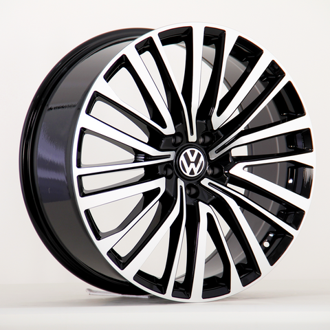 A car wheel features a black and silver multi-spoke design with a central Volkswagen emblem, displayed against a plain white background.