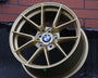 A gold BMW car wheel rim rests upright on a dark surface against a brick wall, displaying the BMW logo at its center.