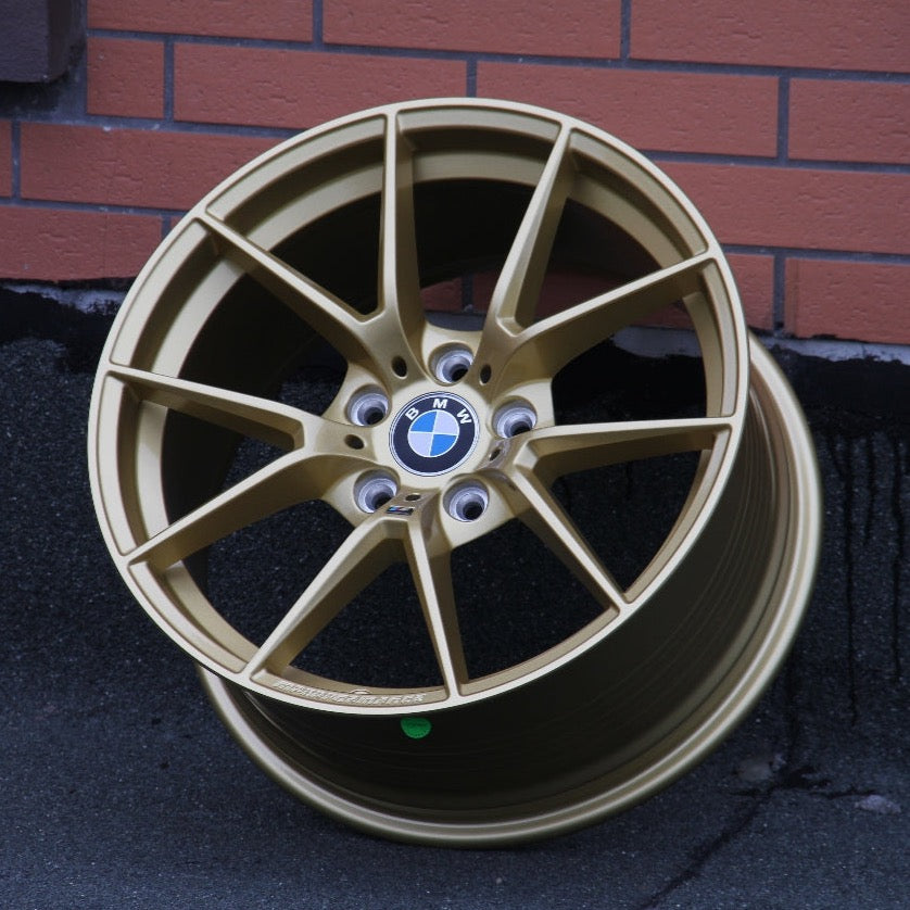 A gold BMW car wheel lies against a brick wall. The wheel is detailed and has a logo at its center. The design is sleek and modern.