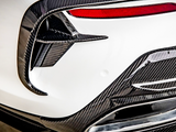 Carbon fiber car detail, featuring aerodynamic fins and trim around a tail light, situated on a white vehicle. The design contributes to a sporty, high-performance appearance.