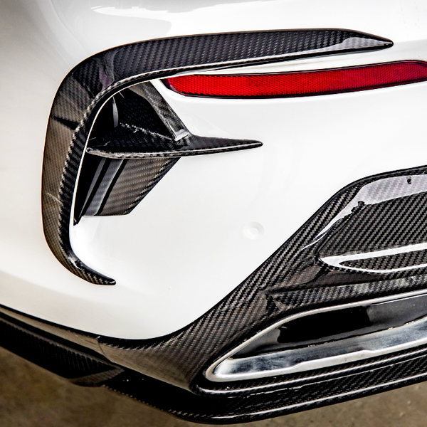 Carbon fiber car detail, featuring aerodynamic fins and trim around a tail light, situated on a white vehicle. The design contributes to a sporty, high-performance appearance.