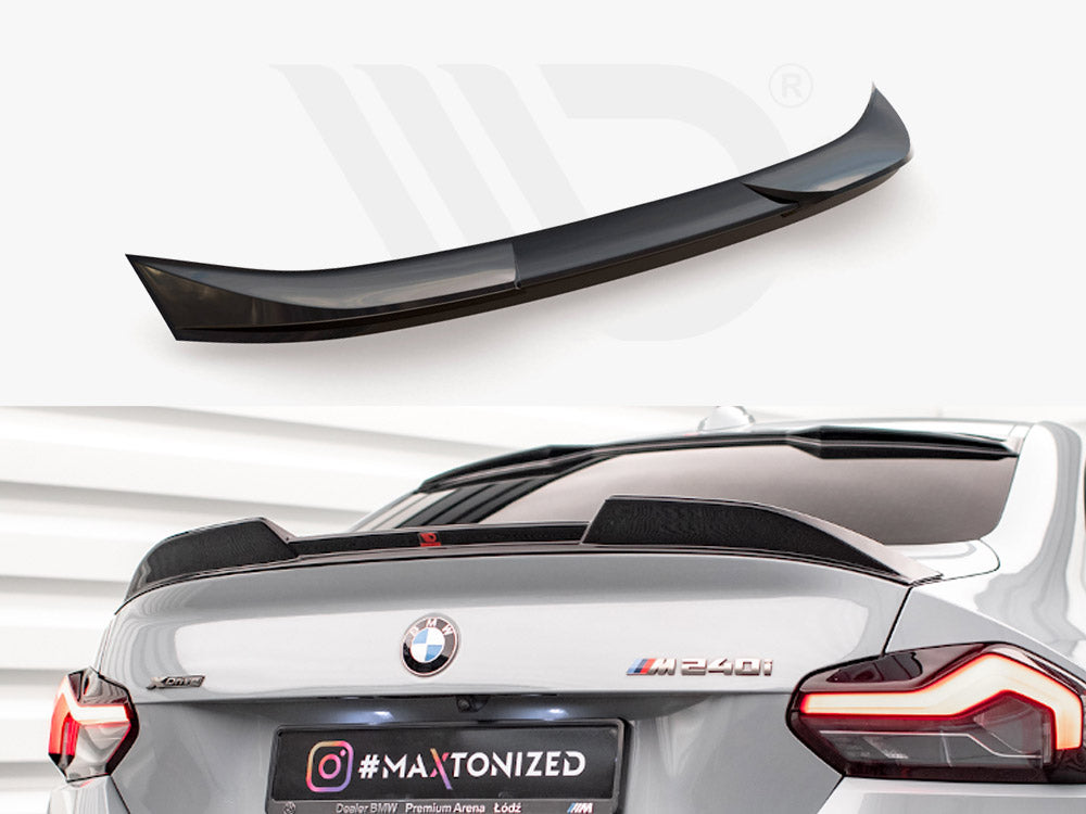 A glossy black rear spoiler sits unattached above a grey BMW M240i in a showroom. Text on the license plate reads "#MAXTONIZED" with an Instagram logo.