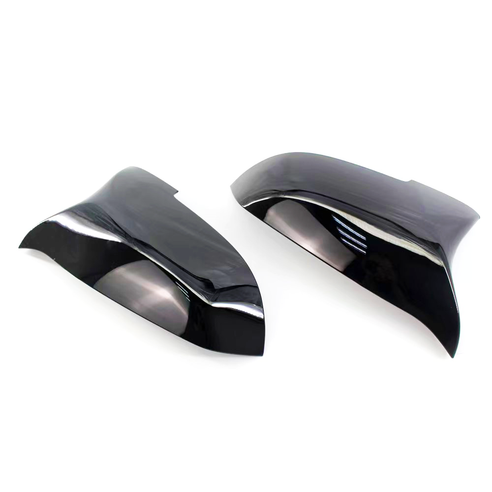 Black, glossy car mirror covers are shown lying side by side on a white background, reflecting light and their smooth, curved design.