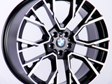 A BMW car wheel rim is displayed against a plain white background, featuring a modern, intricate black and silver geometric design with the BMW logo at the center.