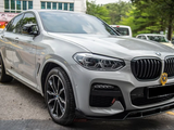 A gray BMW with sleek lines is parked in a lot, surrounded by other vehicles and trees, with a badge on the front grill.