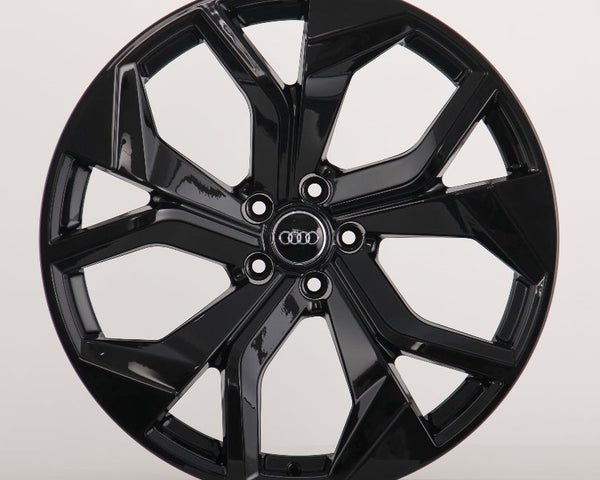 A glossy black alloy wheel with a five-spoke design featuring the Audi logo at the center, sits against a plain white background.