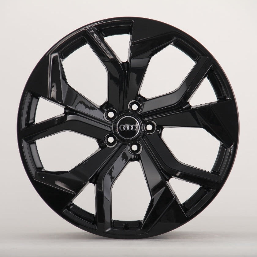 A glossy black alloy wheel with a five-spoke design featuring the Audi logo at the center, sits against a plain white background.