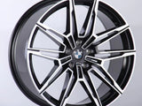 A black and silver multi-spoke alloy car wheel with a BMW logo is positioned upright against a plain white background, showcasing a sleek, modern design.