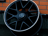 A black alloy wheel with a Mercedes-Benz emblem rests against a brick wall. The text 