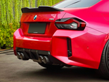 A red BMW M2 car is parked on a driveway, displaying a quad exhaust and black spoiler, with green ivy-covered walls in the background.