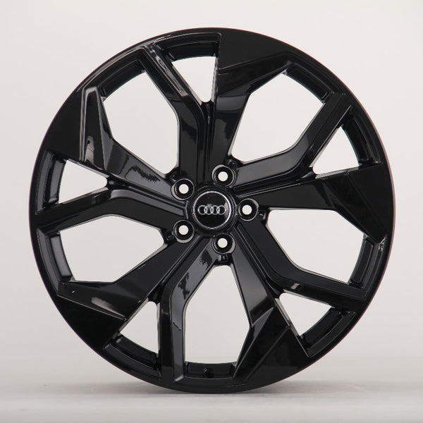 A glossy black alloy wheel with a multi-spoke design. The Audi logo is centered on the hub. It's set against a plain, light grey background.