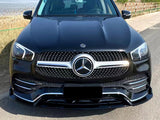 A black Mercedes-Benz SUV is parked on a paved road near a grassy area, with water and industrial structures visible in the background under a clear sky.