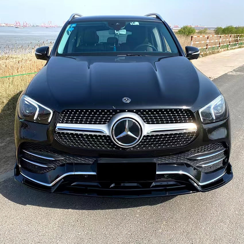 A black Mercedes-Benz SUV is parked on a paved road near a grassy area, with water and industrial structures visible in the background under a clear sky.