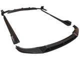 Several carbon fiber car body kit pieces are arranged on a white surface, including a front splitter, side skirts, and a rear diffuser, emphasizing their sleek, aerodynamic design.
