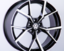A black and silver alloy wheel with a Volkswagen logo in the center is displayed against a plain white background, highlighting the wheel's modern, geometric spoke design.