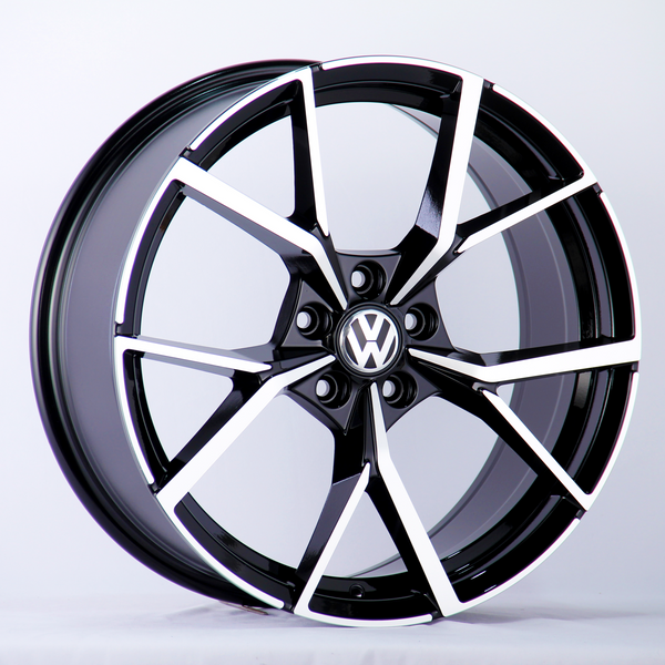 A black and silver alloy wheel with a Volkswagen logo in the center is displayed against a plain white background, highlighting the wheel's modern, geometric spoke design.