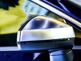 A car's side-view mirror reflects light in a close-up shot, set against the vehicle's shiny blue body and a blurred, yellow-tinted background.