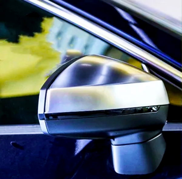 A car's side-view mirror reflects light in a close-up shot, set against the vehicle's shiny blue body and a blurred, yellow-tinted background.
