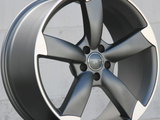 A sleek, metallic alloy wheel with a five-spoke design rests on a flat surface against a plain, light-colored wall background, showcasing its modern, polished appearance.